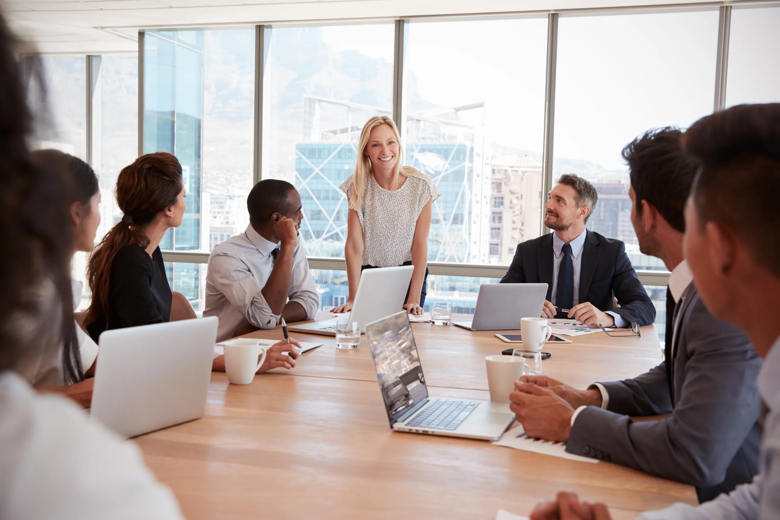 Business meeting in office with individuals sitting around table with laptop computers